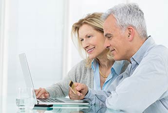 Middle aged couple at a laptop with a debit card